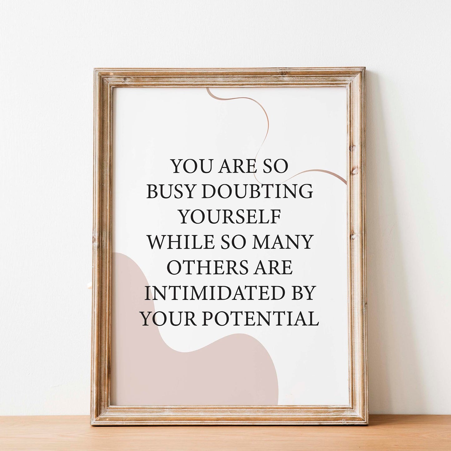 Empowering printable wall art featuring the quote 'You are so busy doubting yourself while so many others are intimidated by your potential' in classic black serif font on a soft beige background with abstract curved shapes, perfect for confidence-boosting home, office, or studio decor