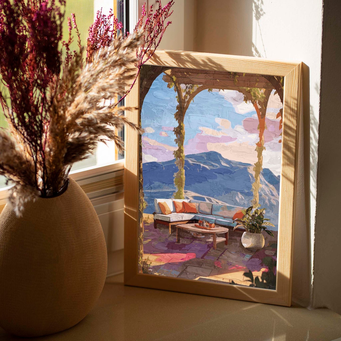 Elegant terrace view wall art featuring a cozy outdoor lounge with colorful cushions, a round coffee table, potted plant, and panoramic mountain scenery under soft sunset skies framed by ivy-covered arches