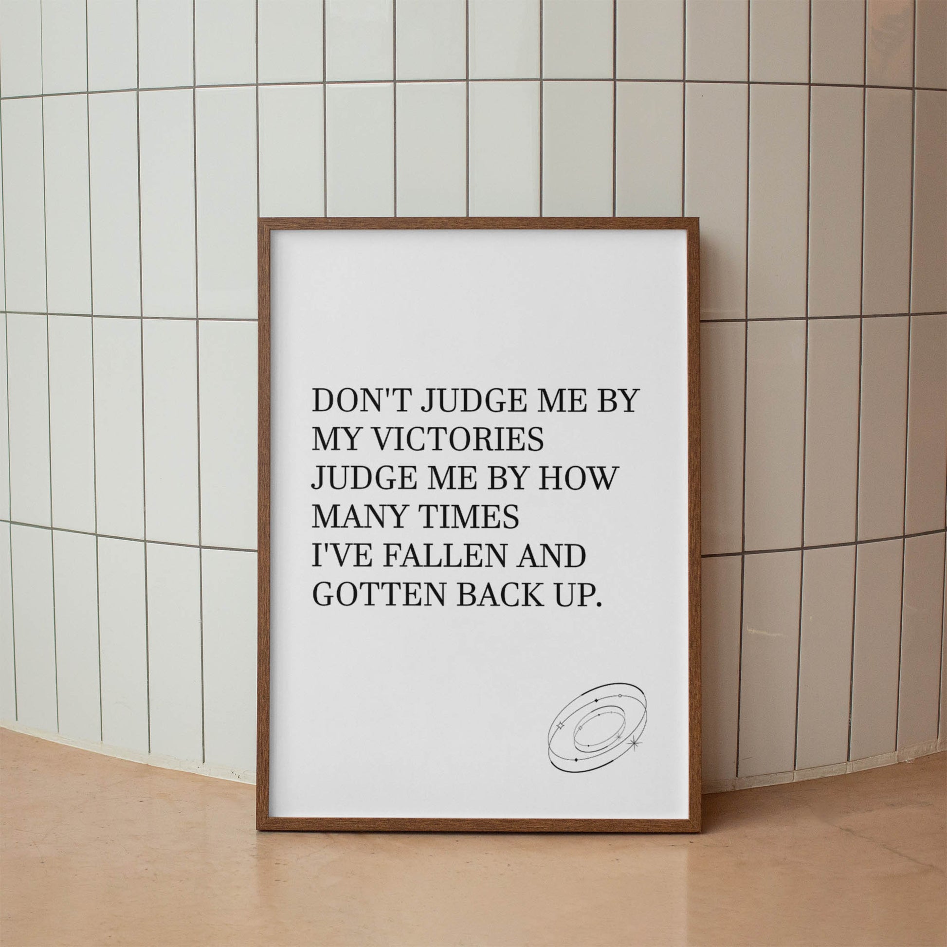 Inspirational printable wall art featuring the empowering quote 'Don't judge me by my victories, judge me by how many times I've fallen and gotten back up' in classic serif font, with a small sketched ring accent, perfect for resilience-themed or motivational spaces.