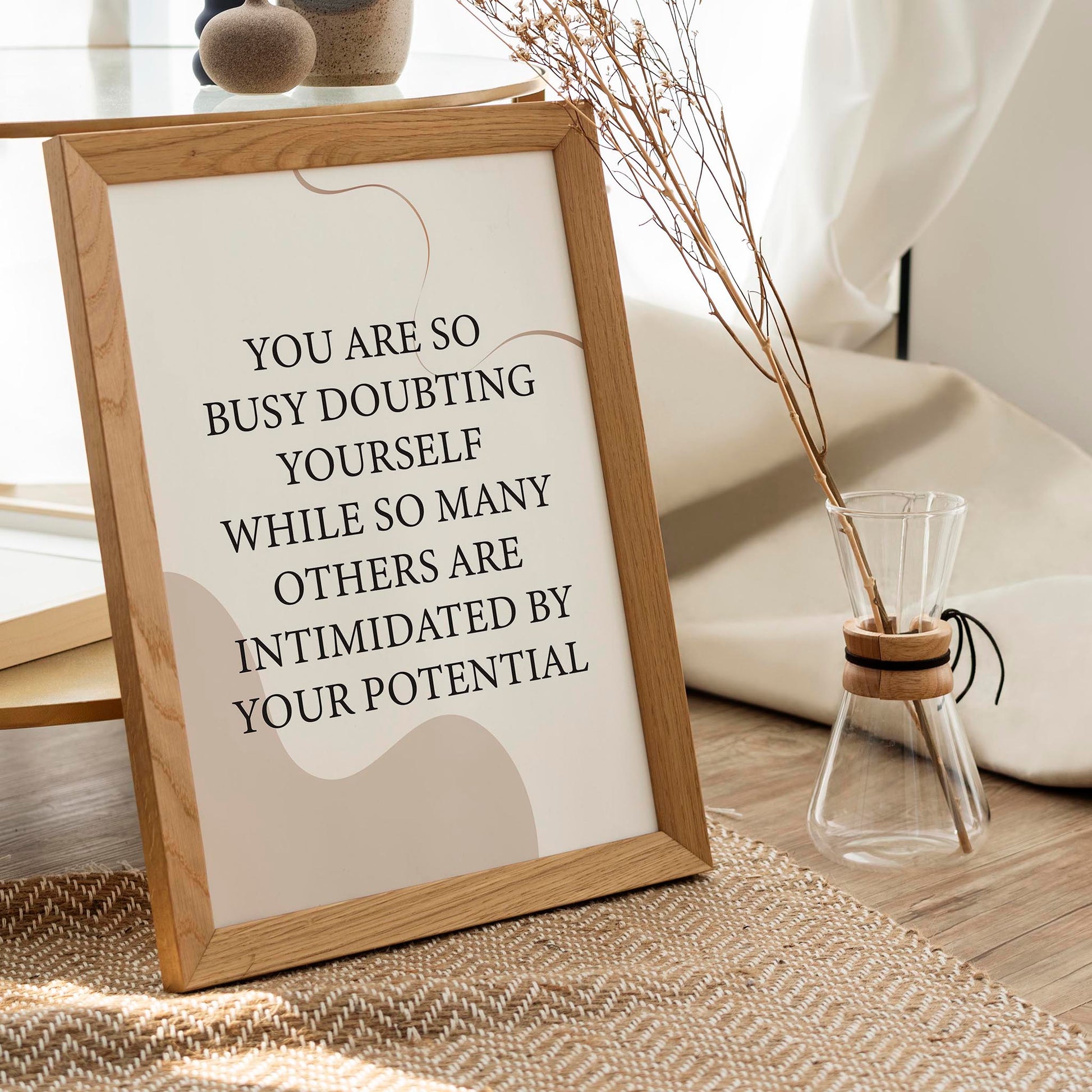 Empowering printable wall art featuring the quote 'You are so busy doubting yourself while so many others are intimidated by your potential' in classic black serif font on a soft beige background with abstract curved shapes, perfect for confidence-boosting home, office, or studio decor