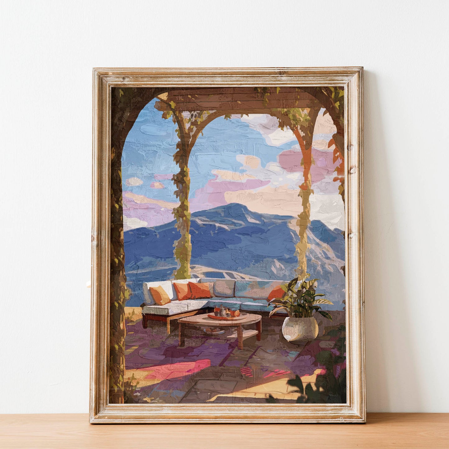 Elegant terrace view wall art featuring a cozy outdoor lounge with colorful cushions, a round coffee table, potted plant, and panoramic mountain scenery under soft sunset skies framed by ivy-covered arches