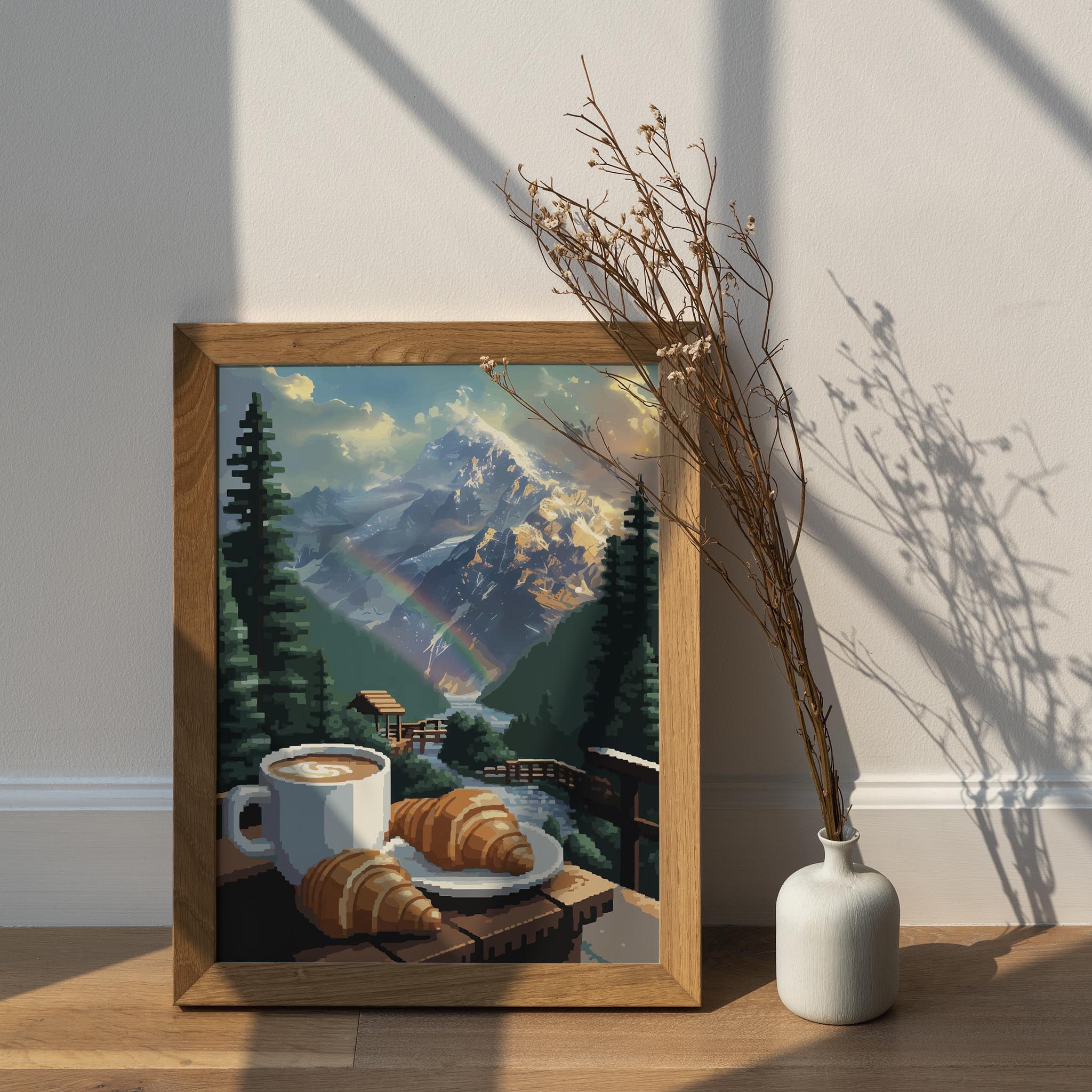 Cozy mountain-themed printable wall art featuring a cup of coffee and croissants on a wooden railing overlooking a flowing stream, lush pine trees, a rainbow, and majestic snow-covered peaks glowing in the morning light - perfect for cabin, breakfast nook, or nature lover decor