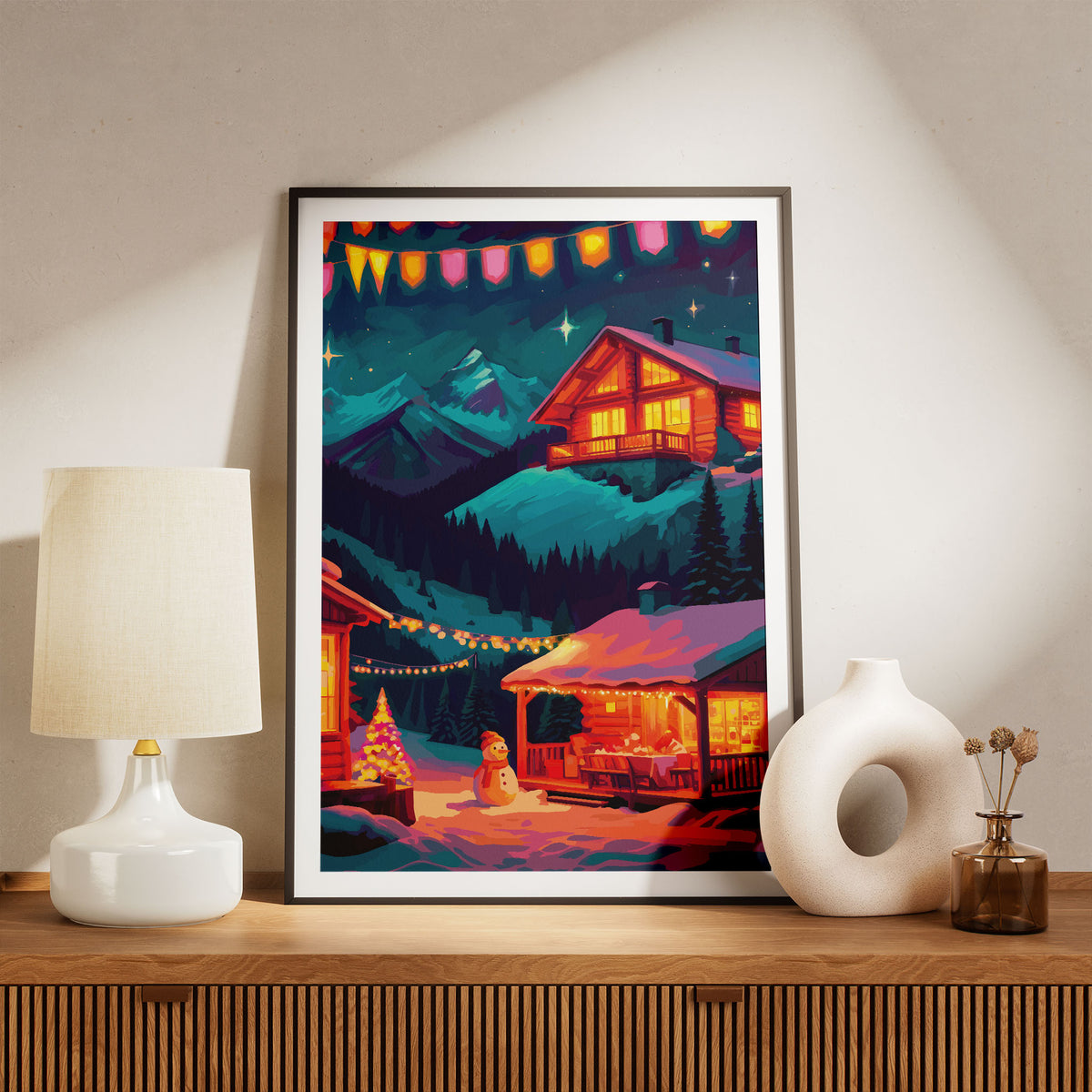 Bold illustrated Christmas village wall art with glowing log cabins on a snowy mountain hillside at night, a snowman beside a lit Christmas tree, string lights strung between buildings, colourful bunting, and a deep teal starry sky with bright diamond stars