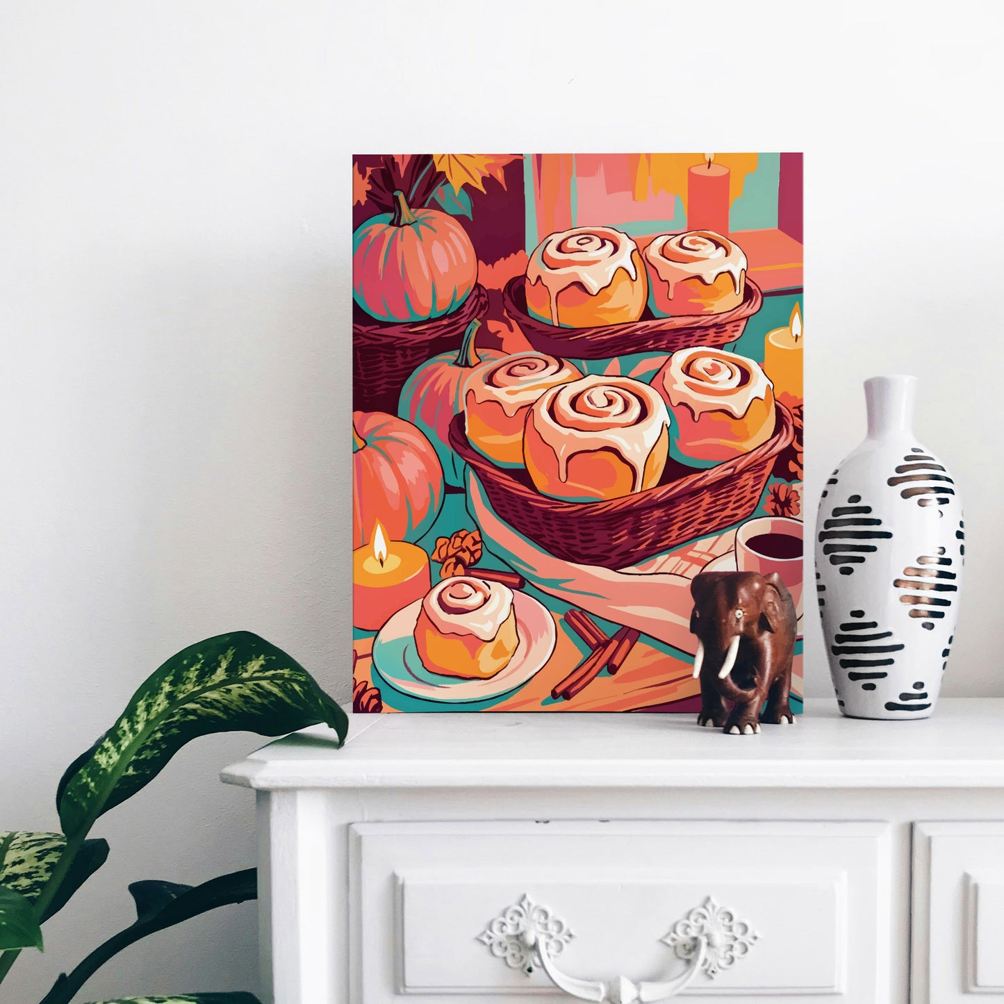 Cozy fall baking print featuring close-up illustrated cinnamon rolls with dripping cream cheese icing, set on a teal table with candles, pumpkins, and pine cones