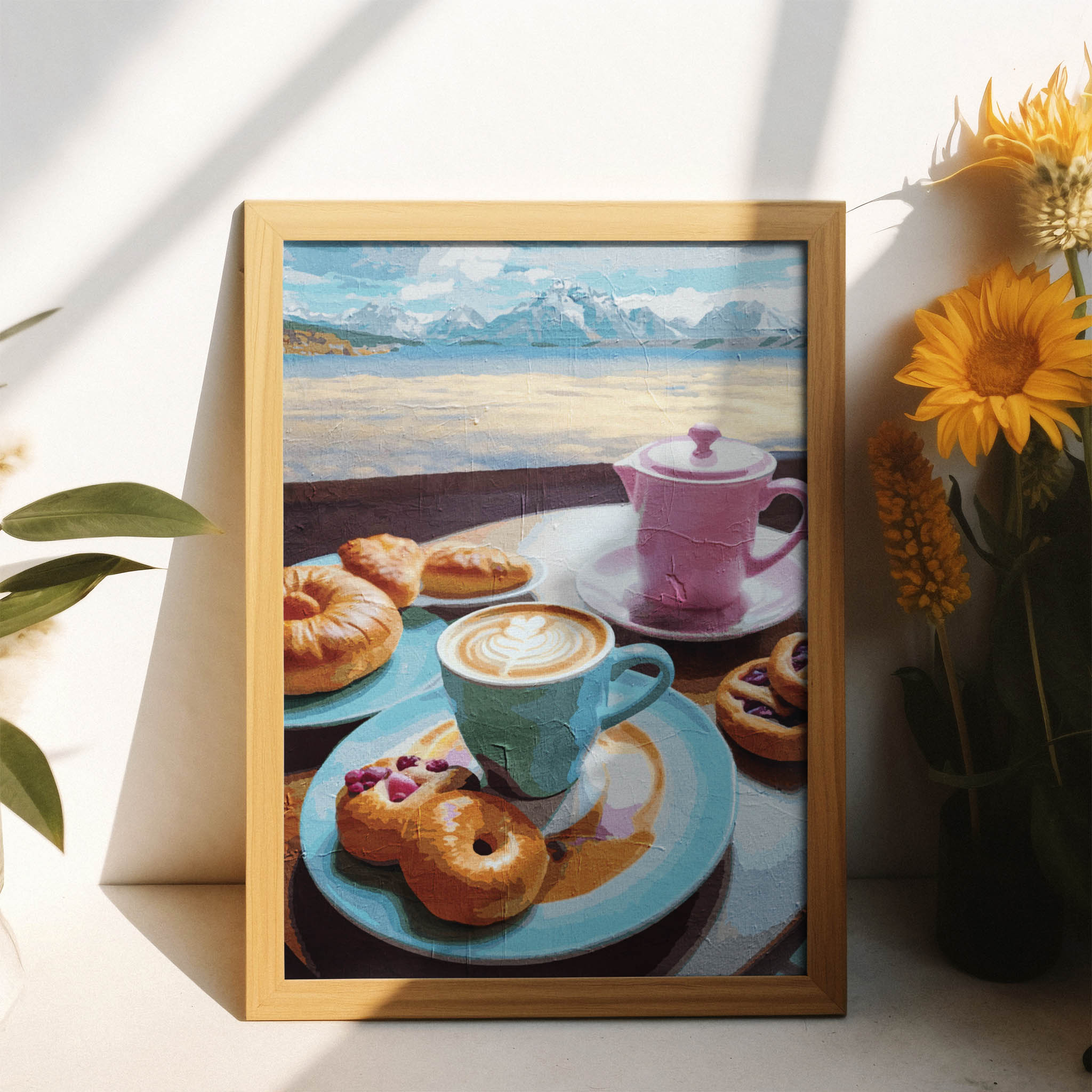 Printable wall art of a charming breakfast scene with a blue coffee cup, pink teapot, assorted pastries, and donuts on colorful plates, set against a scenic backdrop of mountains and water, perfect for kitchen or café-inspired decor.