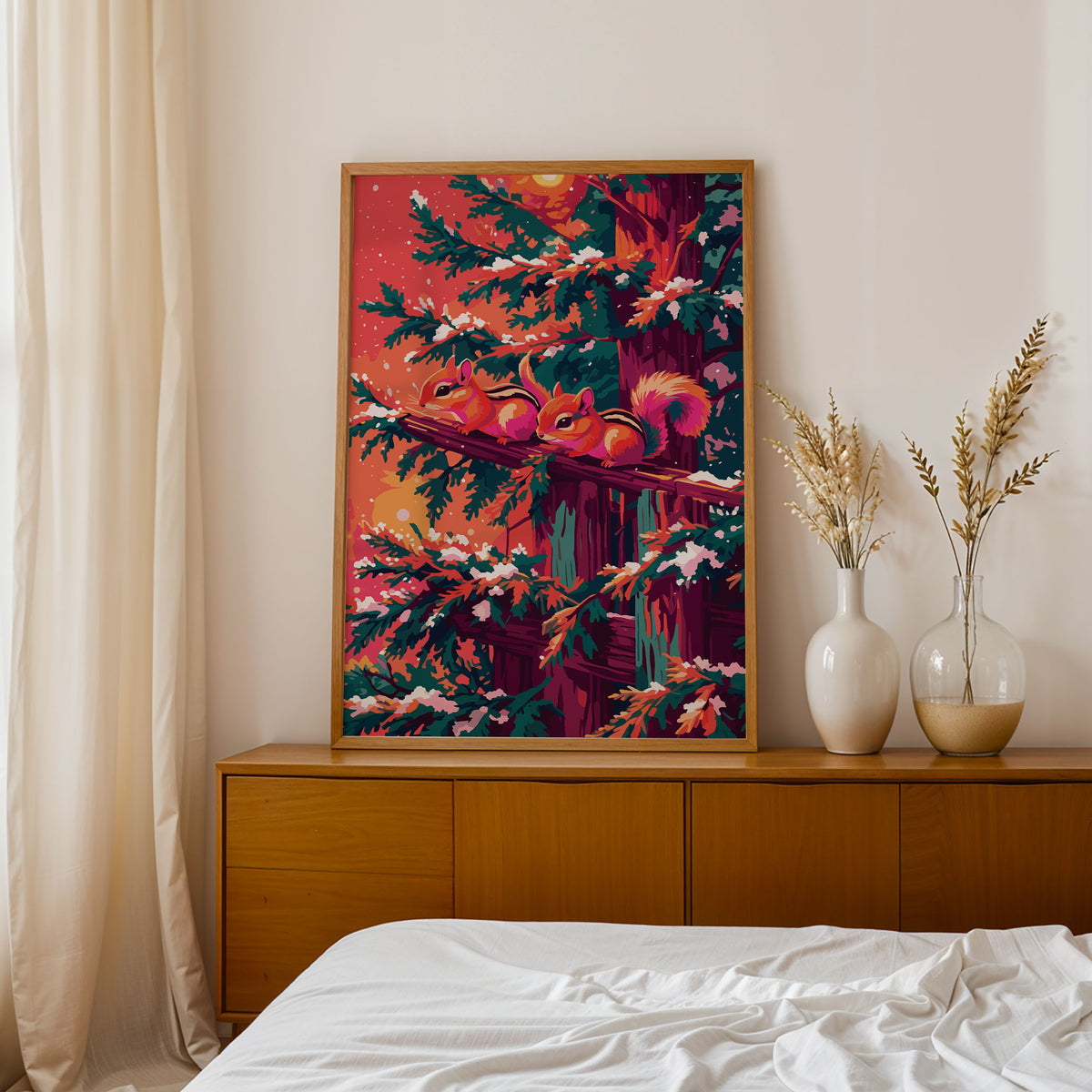 Bold illustrated winter wall art with two chipmunks perched nose-to-nose on a snow-dusted wooden railing, surrounded by teal pine branches heavy with snow against a warm coral and orange winter sky