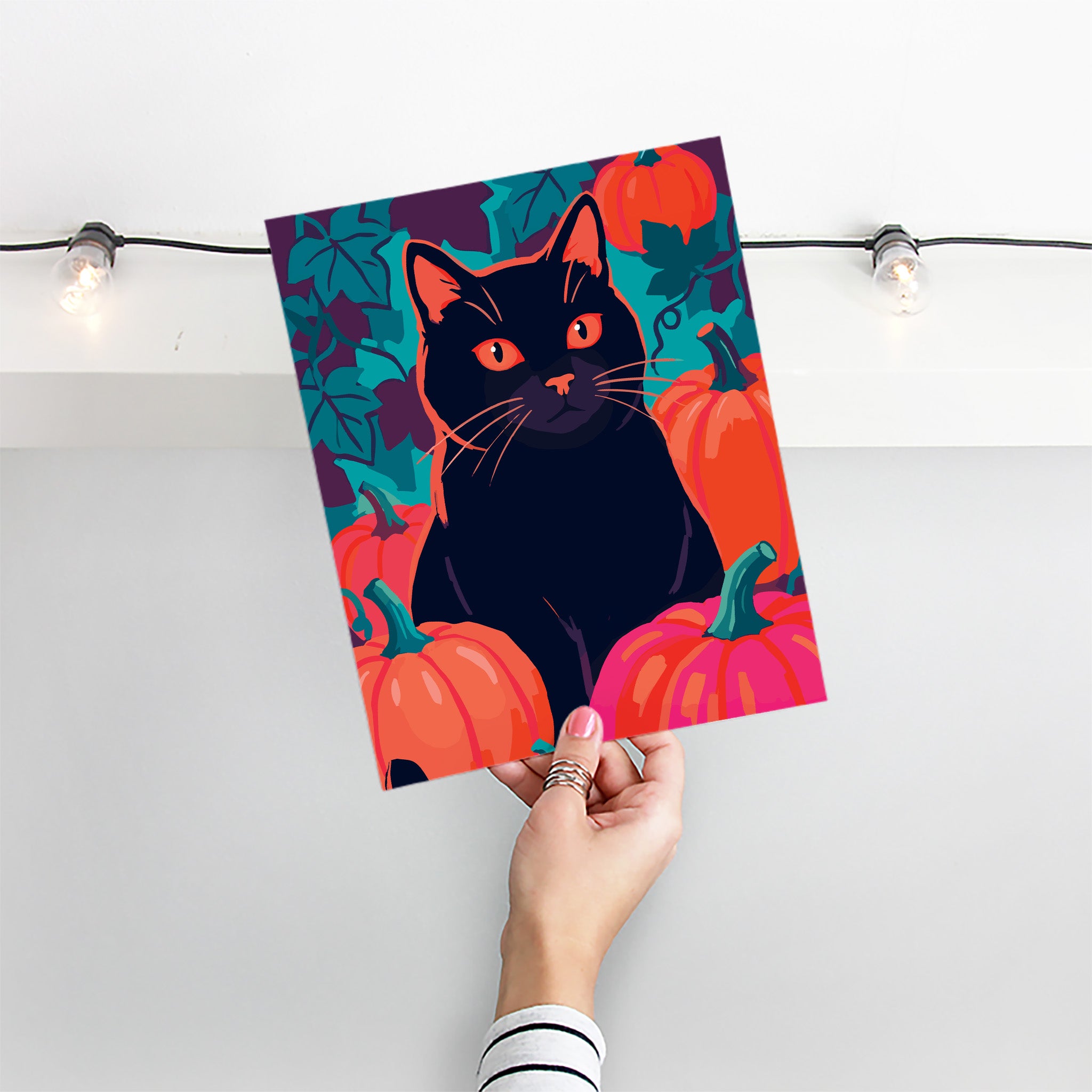 Close-up of a striking Halloween animal print - a black cat with vivid orange-red eyes and orange whisker highlights sits directly among pumpkins in orange and hot pink with teal stems against a moody teal vine background
