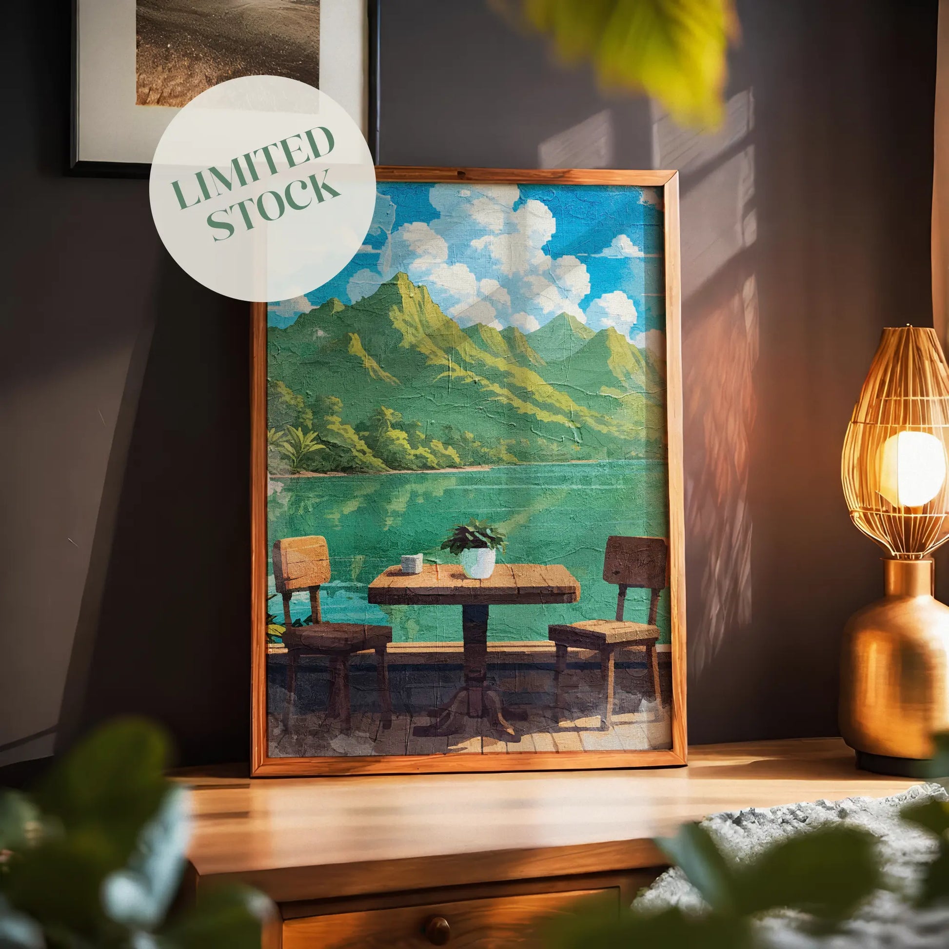 Tropical lakefront printable wall art featuring a rustic wooden table with two chairs overlooking calm turquoise water and lush green mountains under a bright blue sky with fluffy clouds - perfect for vacation-inspired, outdoor dining, or serene nature-themed decor