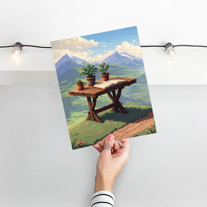 Scenic mountain view printable wall art featuring a rustic wooden table with potted plants and an open book, set against a breathtaking backdrop of lush green valleys and snow-capped peaks under a bright blue sky