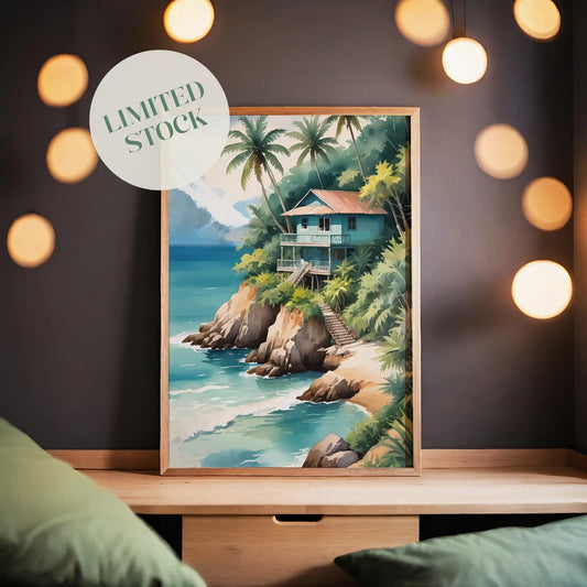Tropical beach wall art of a wooden house on a cliff surrounded by palm trees, overlooking turquoise ocean waves with mountains in the background