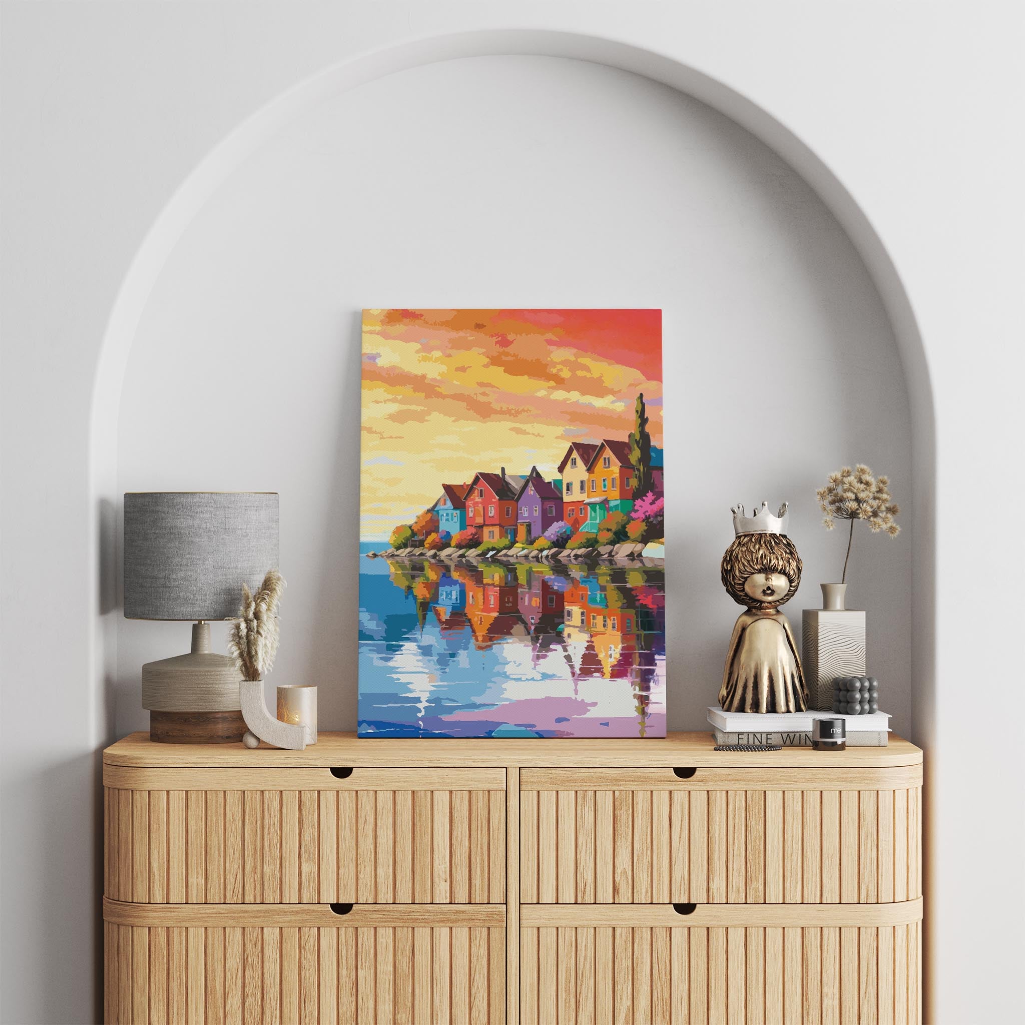 Colorful coastal village wall art featuring charming rainbow-hued houses reflected in calm water, set against a warm, golden sunset sky with vibrant orange and pink clouds