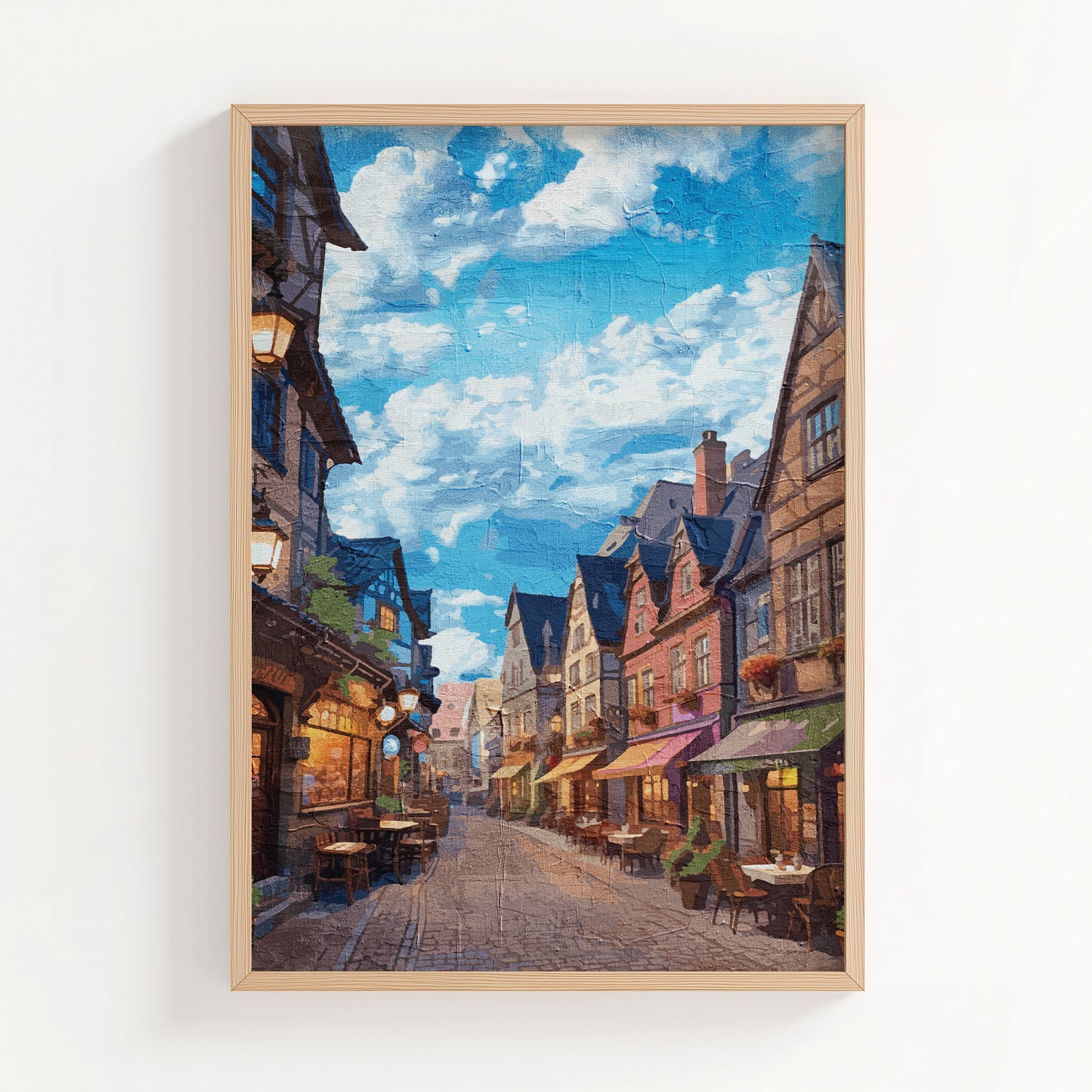 Cozy European village street wall art depicting a cobblestone alley lined with colorful historic buildings, quaint outdoor cafés, and warm lights under a vibrant blue sky with scattered clouds