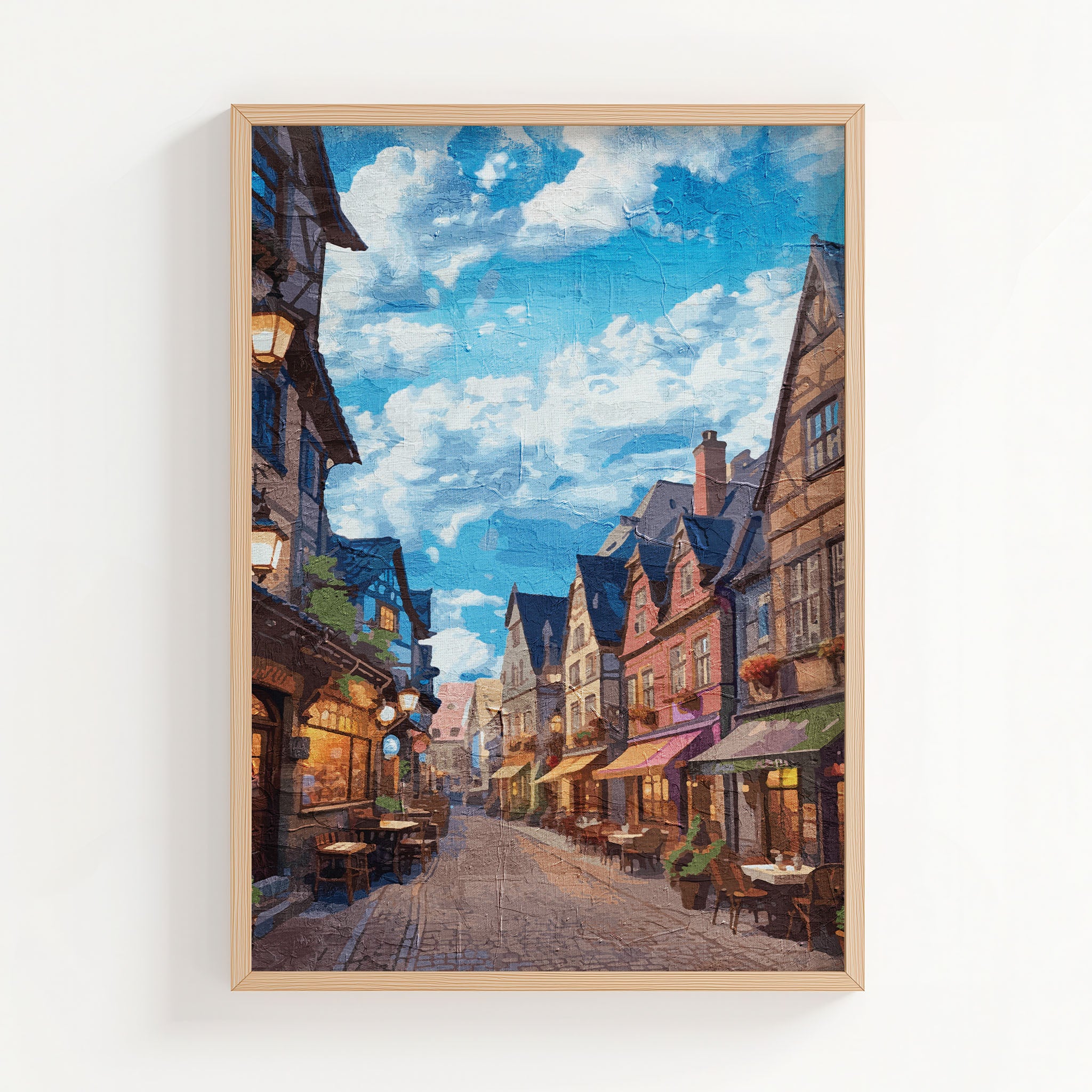Cozy European village street wall art depicting a cobblestone alley lined with colorful historic buildings, quaint outdoor cafés, and warm lights under a vibrant blue sky with scattered clouds
