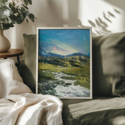 Rustic mountain valley wall art featuring a flowing stream winding through grassy hills and rocky terrain, with forested slopes and a soft, colorful sky above the distant peaks