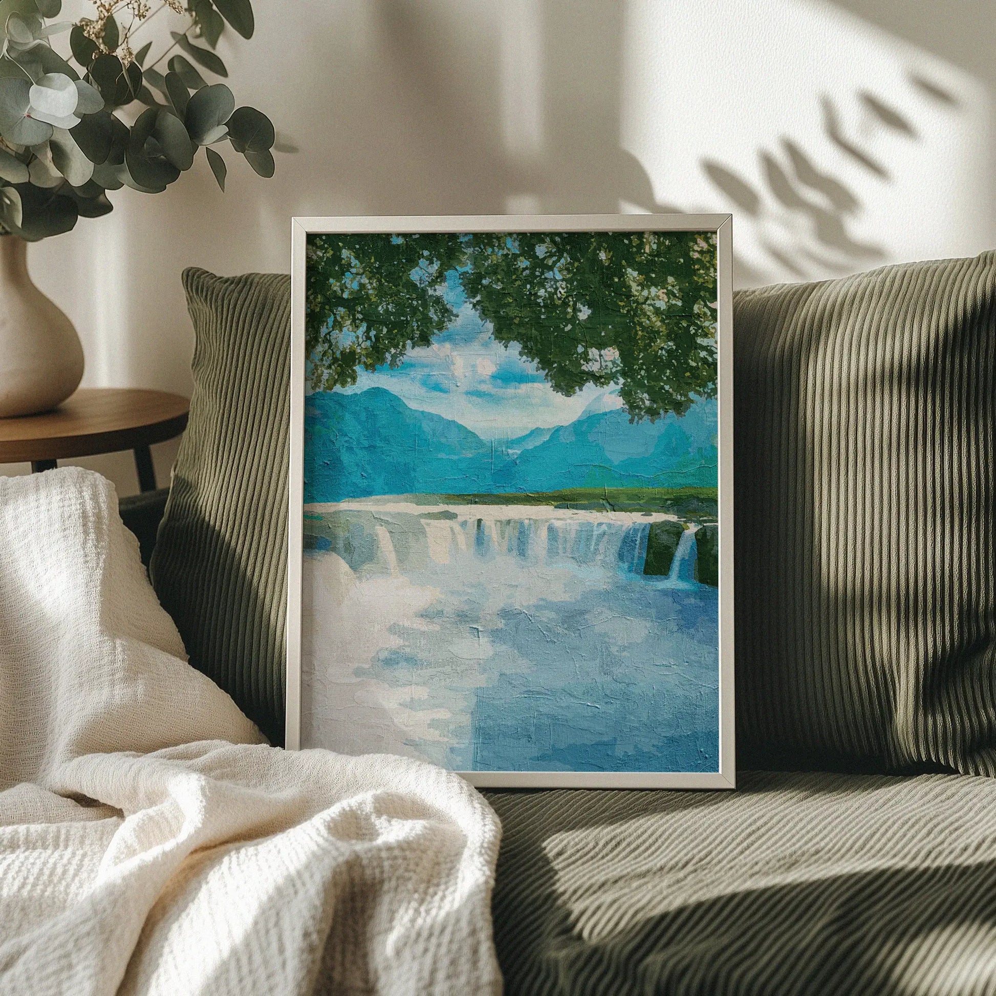 Tranquil waterfall wall art featuring a wide, gentle cascade framed by leafy tree branches, with distant blue mountains and a peaceful sky creating a calming nature scene