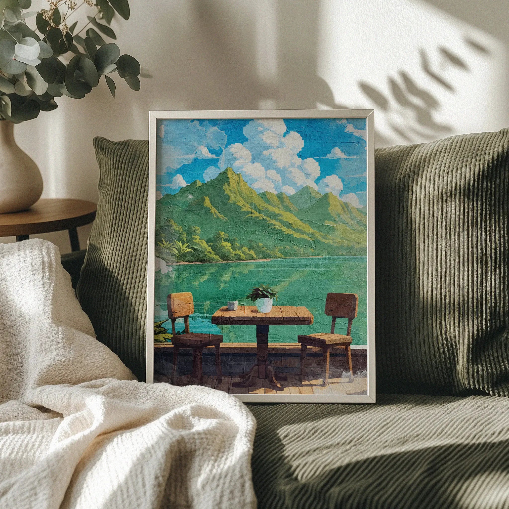 Tropical lakefront printable wall art featuring a rustic wooden table with two chairs overlooking calm turquoise water and lush green mountains under a bright blue sky with fluffy clouds - perfect for vacation-inspired, outdoor dining, or serene nature-themed decor