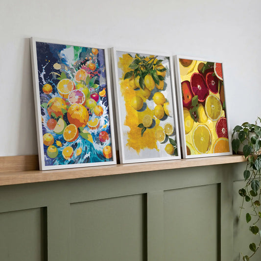 Set of three framed citrus fruit prints displayed on a wooden shelf featuring oranges, lemons and grapefruit in vibrant colours