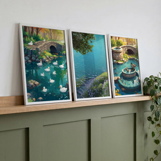 Set of three framed landscape prints displayed on a wooden shelf featuring a duck pond, lake view and garden fountain scene