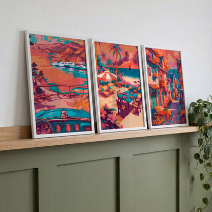 Gallery wall trio featuring a mountain bay, a tropical patio with umbrella and table, and a colorful town street, in warm coral and pink hues.