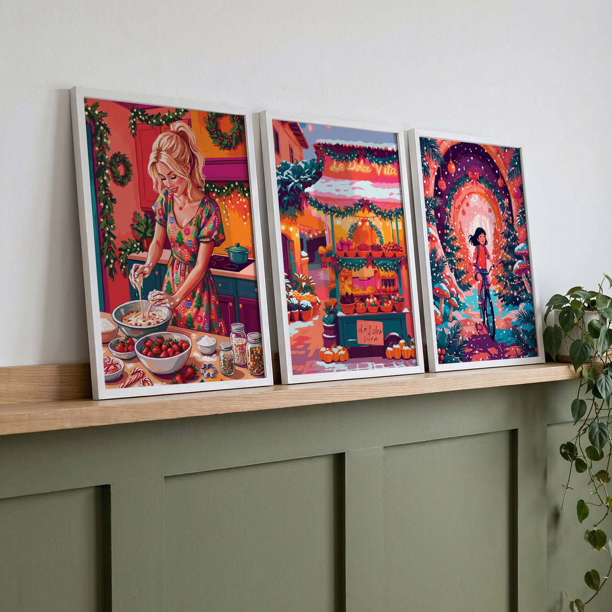Set of three colorful holiday wall art prints displayed on a wooden shelf above a green console