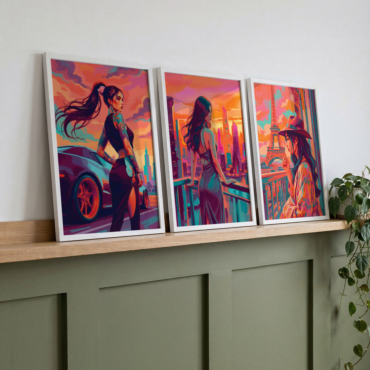 Dreamy Portraits wall art prints on a wood shelf against sage green panelling — a tattooed woman beside a sports car, a woman in a backless dress overlooking a futuristic skyline, and a woman in a wide-brim hat at the Eiffel Tower in vivid orange, teal, and magenta