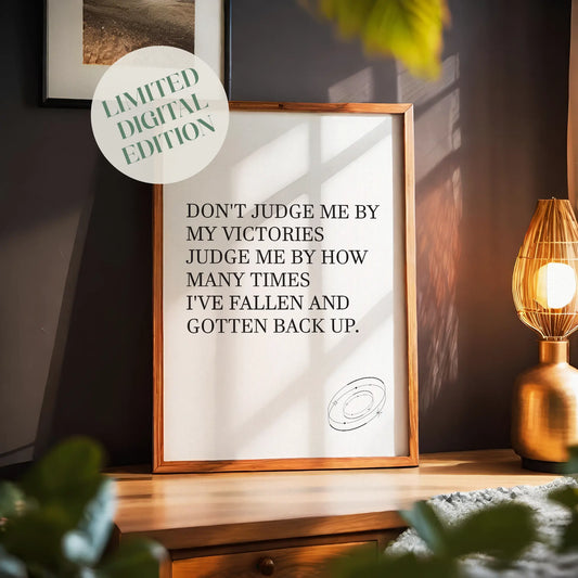 Inspirational printable wall art featuring the empowering quote 'Don't judge me by my victories, judge me by how many times I've fallen and gotten back up' in classic serif font, with a small sketched ring accent, perfect for resilience-themed or motivational spaces.